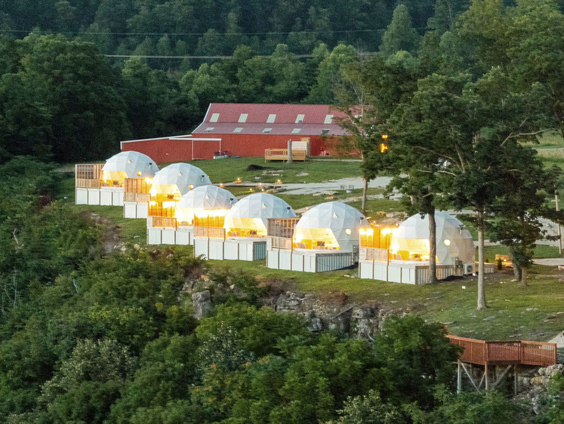 Warmly lit geodesic domes lining the ridgetop at dusk above the forested Red River Gorge valley